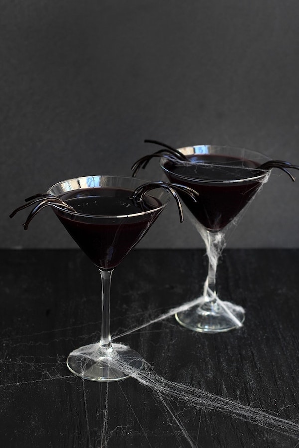 Black licorice widow martini made with black vodka, Jägermeister, and blueberry‑pomegranate juice with licorice string bug "legs" for a garnish.