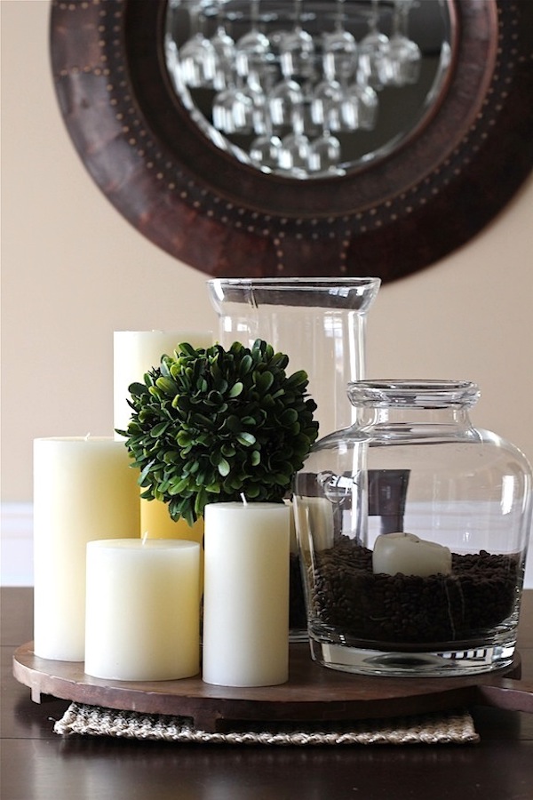 Glass hurricane vase filled with whole coffee beans surrounding a pillar candle for an easy DIY fall centerpiece.