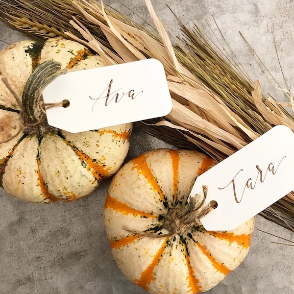 Mini white pumpkins with handwritten name tags tied on with twine for DIY Thanksgiving place cards.