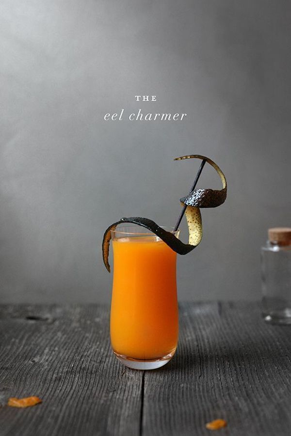 Eel charmer cocktail made with bourbon, honey, orange juice, and a splash of blood orange Italian soda and garnished with an orange peel made to look like eel skin.