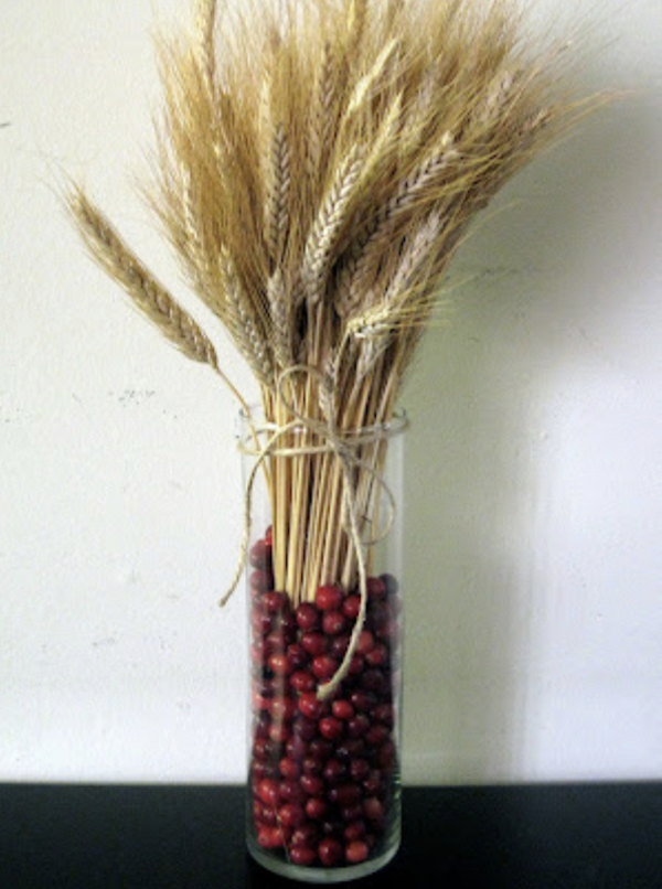 Glass vase filled with cranberries and decorative wheat for a simple DIY Thanksgiving centerpiece.
