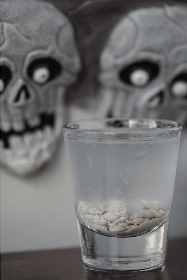 Zombie shooter in a shot glass with two spooky skull decorations in the background.