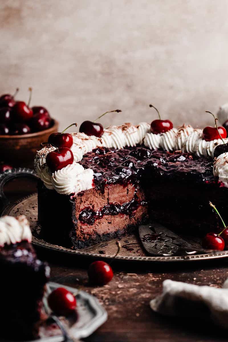 Black forest cheesecake with Oreo crust, chocolate cheesecake filling, a ripple of cherry sauce baked through the center, and whipped cream and fresh cherries on the top.