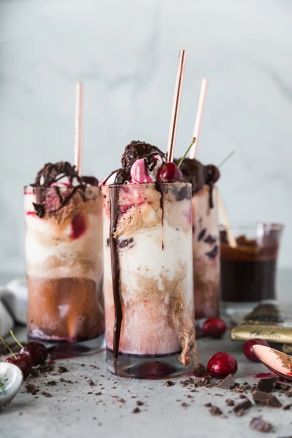 Dark chocolate cherry bourbon float topped with whipped cream, chocolate fudge sauce, and fresh cherries in a tall glass.