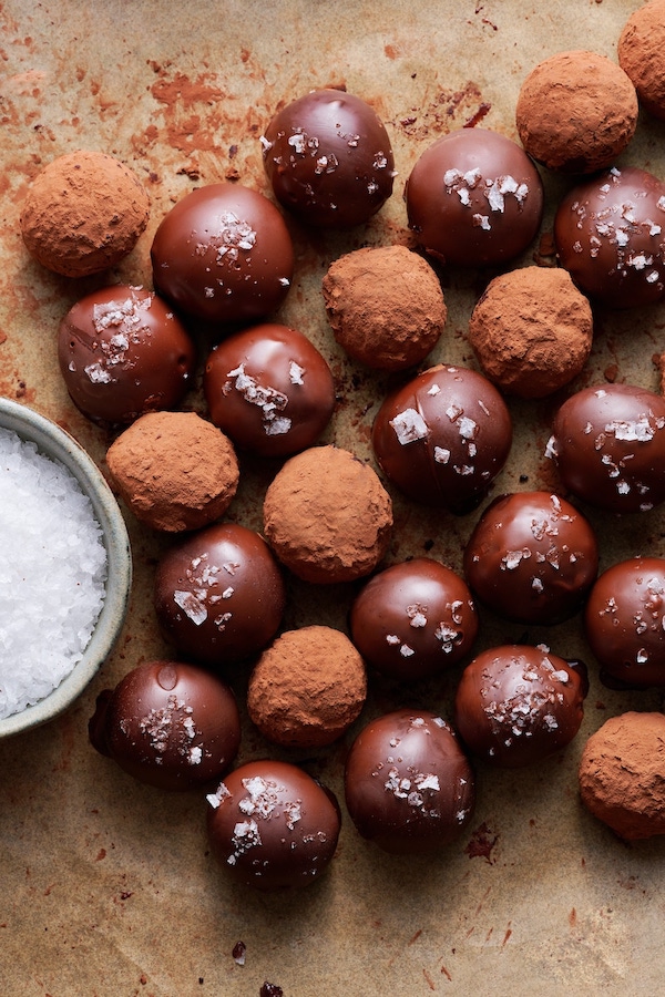 Dark chocolate Grand Marnier truffles coated in chocolate and cocoa powder, topped with flaky sea salt, on a parchment-lined baking sheet.