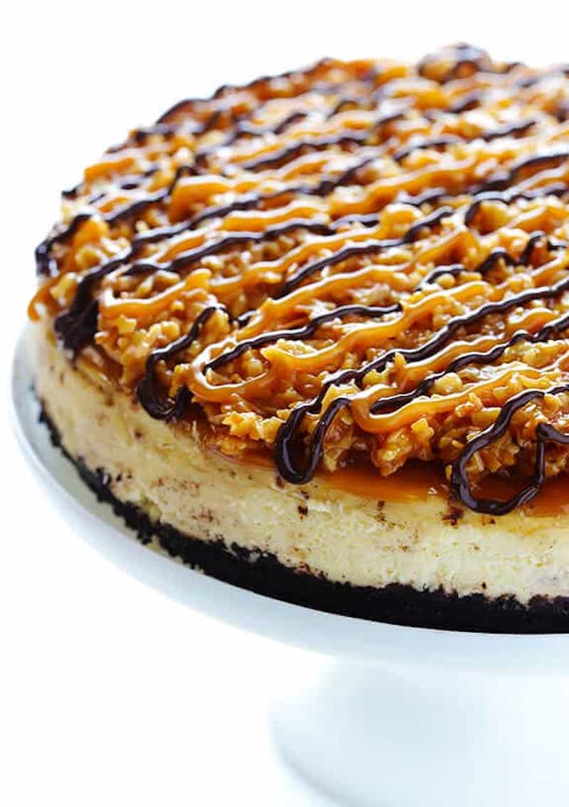 Samoa cheesecake with an Oreo cookie crust topped with caramel, toasted coconut, and a chocolate drizzle.
