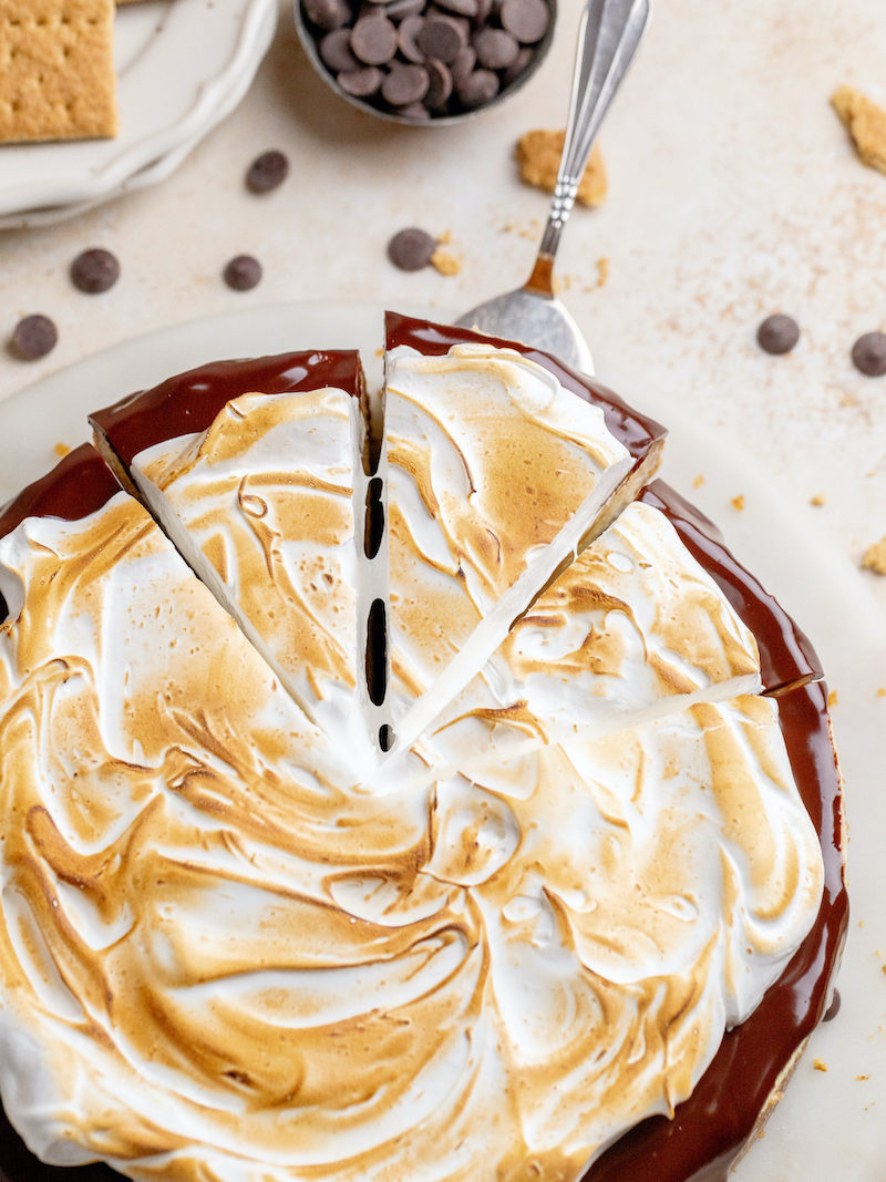 S'mores cheesecake featuring creamy vanilla cheesecake and graham cracker crust topped with dark chocolate ganache and toasted meringue.