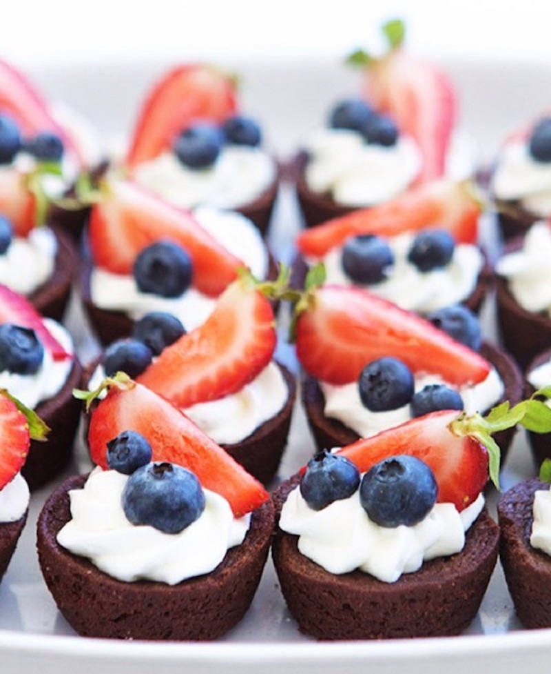 Brownie bites topped with homemade whipped cream, fresh strawberries, and blueberries for an easy red, white, and blue 4th of July dessert.