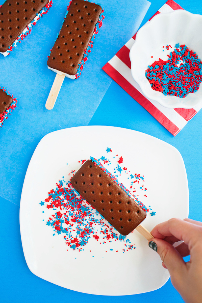 Store-bought ice cream sandwiches dipped in red, white, and blue sprinkles and served on popsicle sticks for an easy patriotic 4th of July dessert.