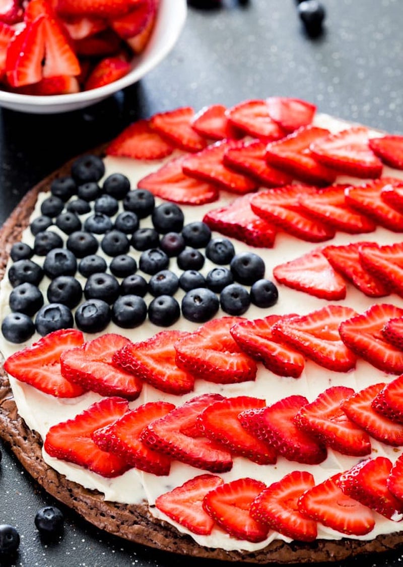 Brownie pizza topped with cream cheese frosting, fresh strawberries, and blueberries arranged in an American flag design for a patriotic 4th of July dessert.