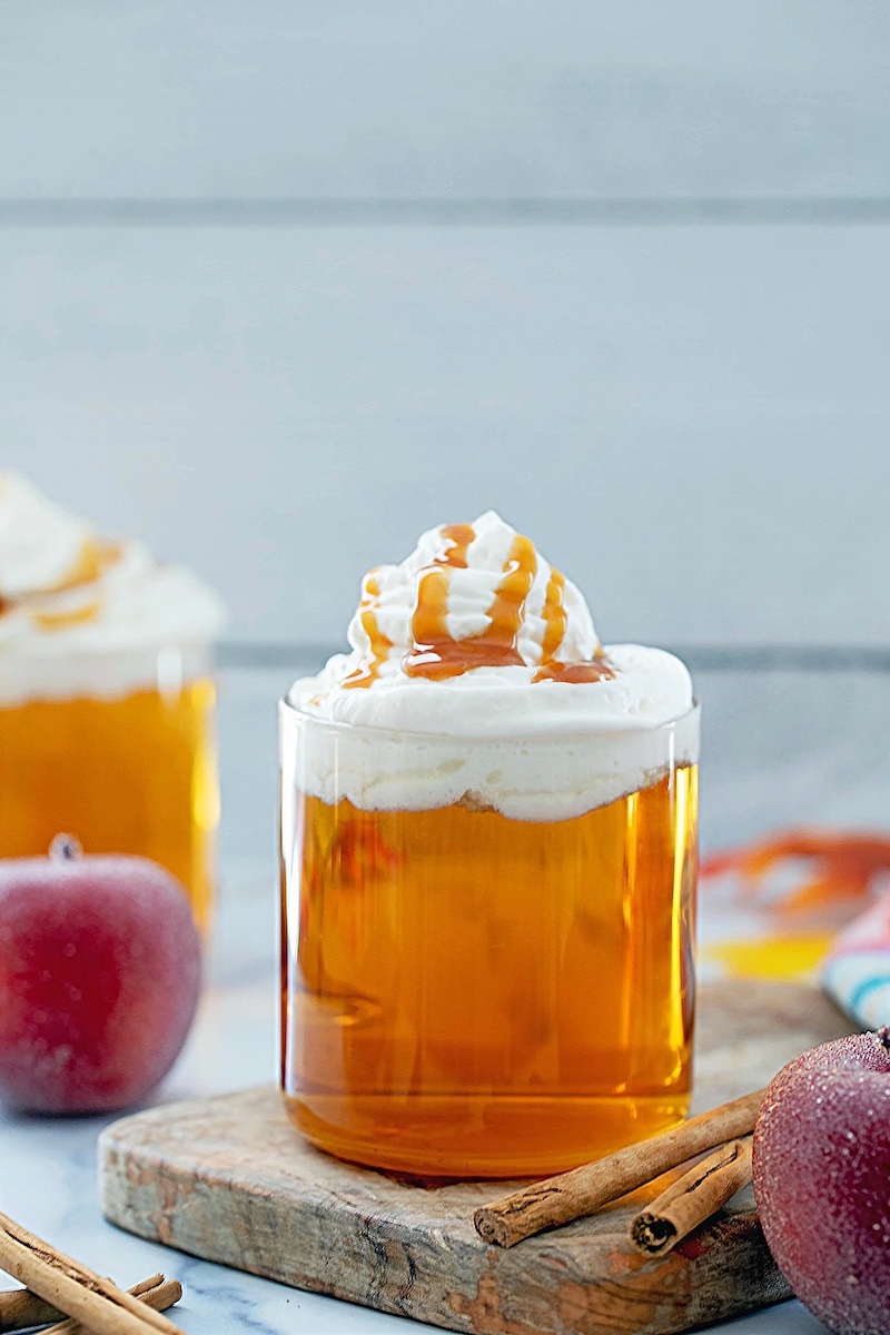 Starbucks Caramel Apple Spice topped with whipped cream and caramel sauce in a clear glass mug.