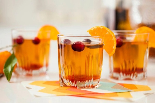 Three glasses of wild turkey cocktail garnished with fresh cranberries and orange slices.
