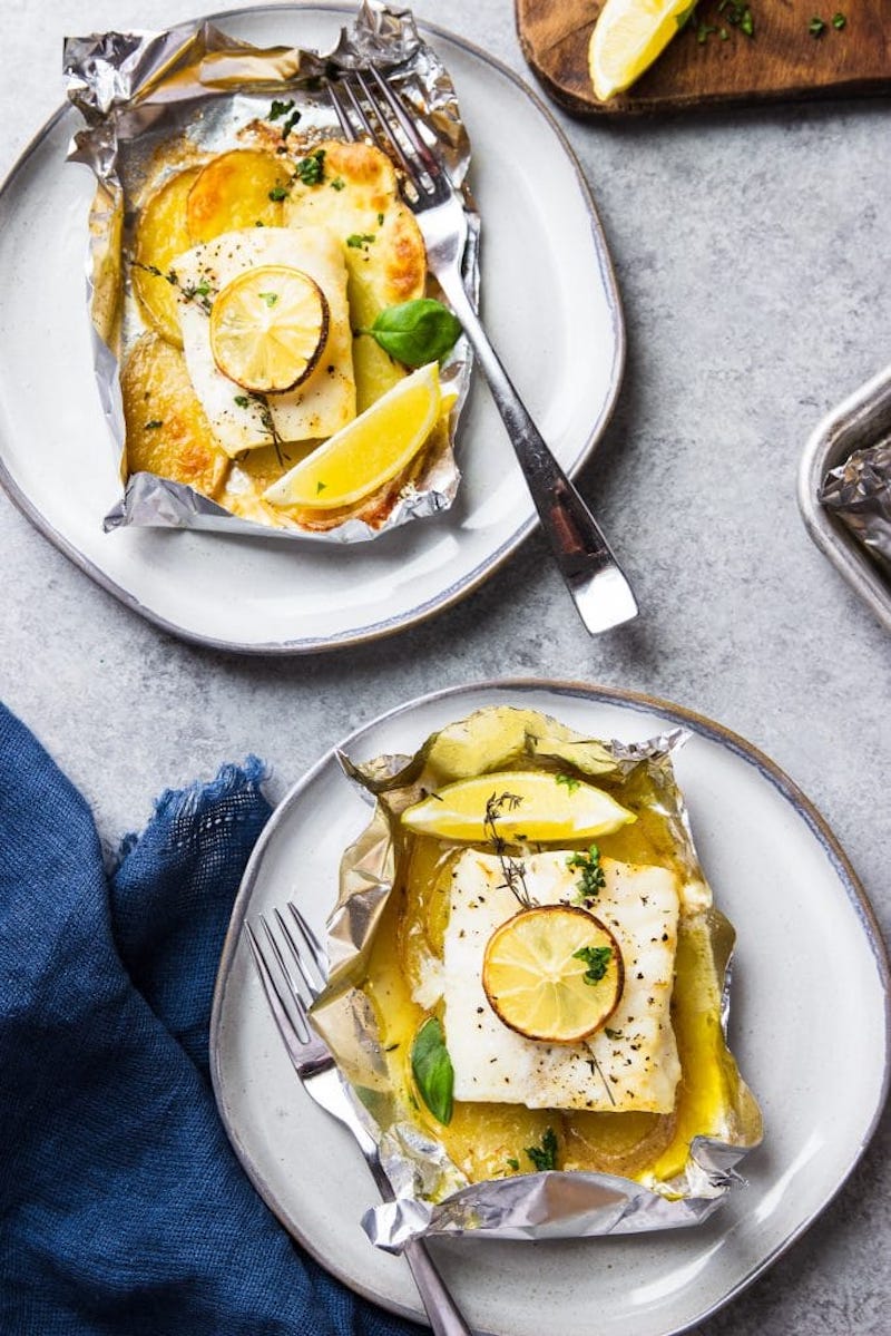 Cod baked in a foil packet with buttery sliced potatoes, lemon, and fresh thyme served on a plate.