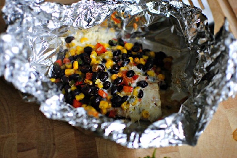 Tilapia foil packet with black beans, sweet corn, red bell pepper, pepper jack cheese, and cilantro cooked in aluminum foil.