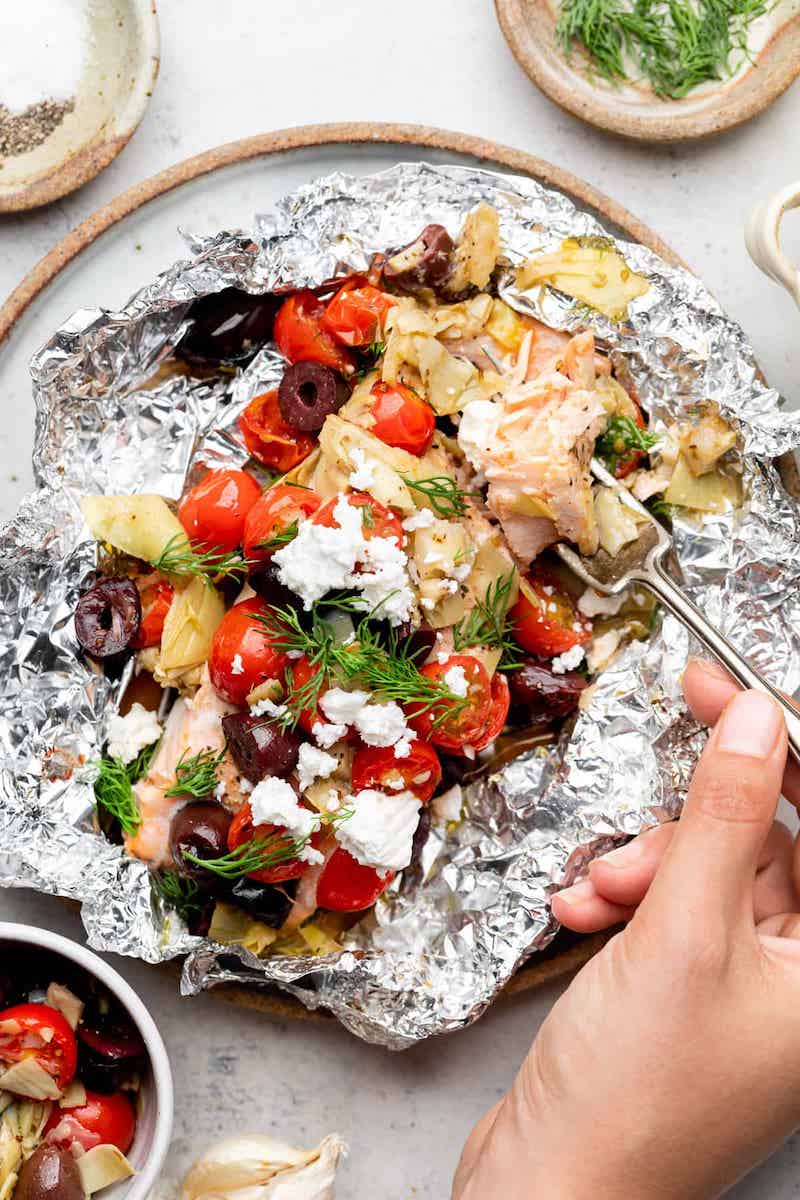 Mediterranean salmon foil packet with cherry tomatoes, Kalamata olives, artichokes, feta cheese, fresh dill, and lemon cooked in aluminum foil.