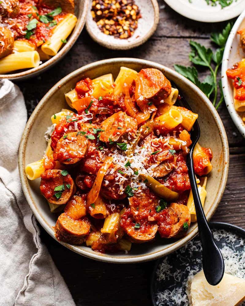 Overhead view of sausage and peppers with parmesan served over rigatoni pasta in a bowl.