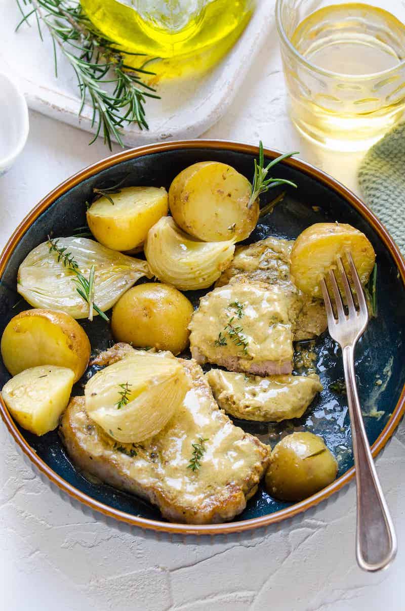 Overhead view of mustard pork chops with baby potatoes, onion, and rosemary on a blue plate.
