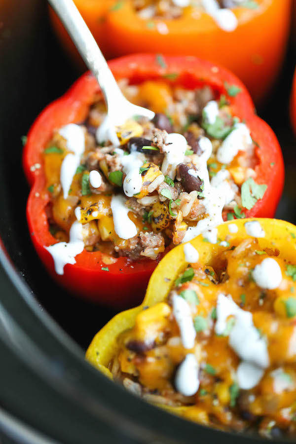 A closeup of slow cooker stuffed peppers still in the Crockpot with a drizzle of sour cream on top.
