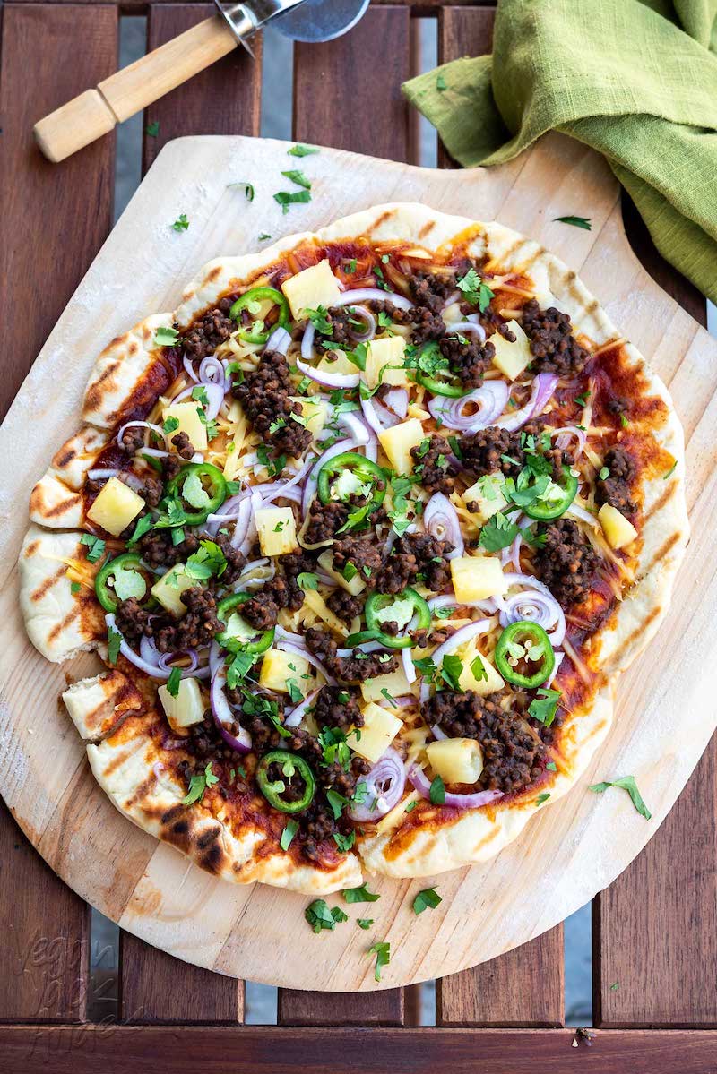 Fire-cooked pizza loaded with BBQ lentils, vegan cheese, pineapple, and jalapeños.