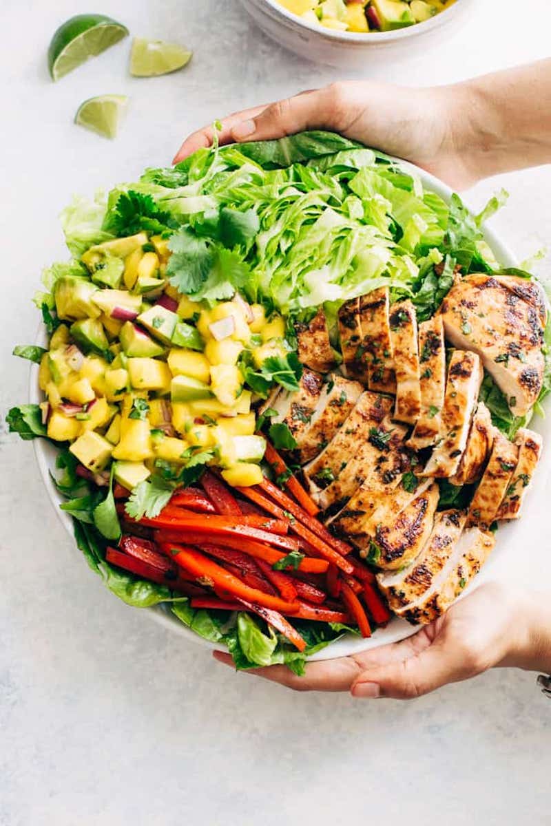 Fiesta Chili Lime Chicken Salad with grilled chicken, mango avocado salsa, sautéed red peppers, romaine lettuce, and fresh cilantro in a large white serving bowl.