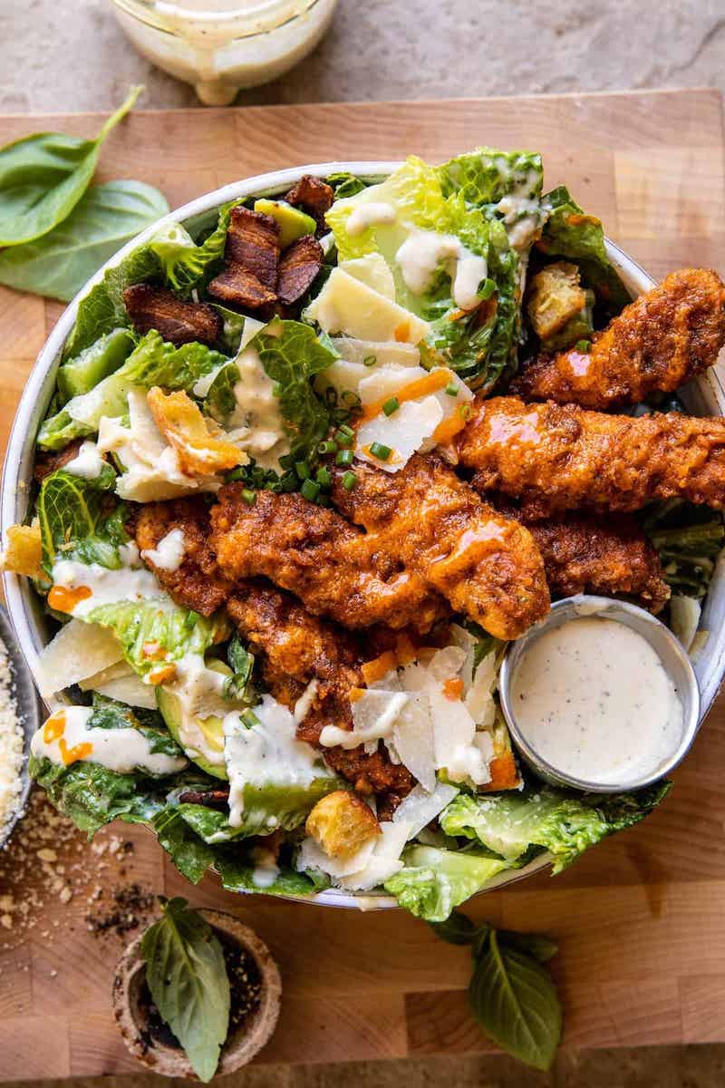 Buffalo Ranch Pretzel Chicken Caesar Salad with crispy buffalo chicken, romaine lettuce, avocado, bacon, Parmesan cheese, croutons, and creamy Caesar dressing in a large bowl.