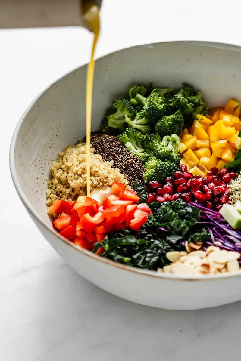 Superfood salad made with kale, spinach, quinoa, broccoli, bell peppers, green apple, pomegranate seeds, almonds, hemp seeds, and chia seeds, drizzled with a homemade maple Dijon dressing.