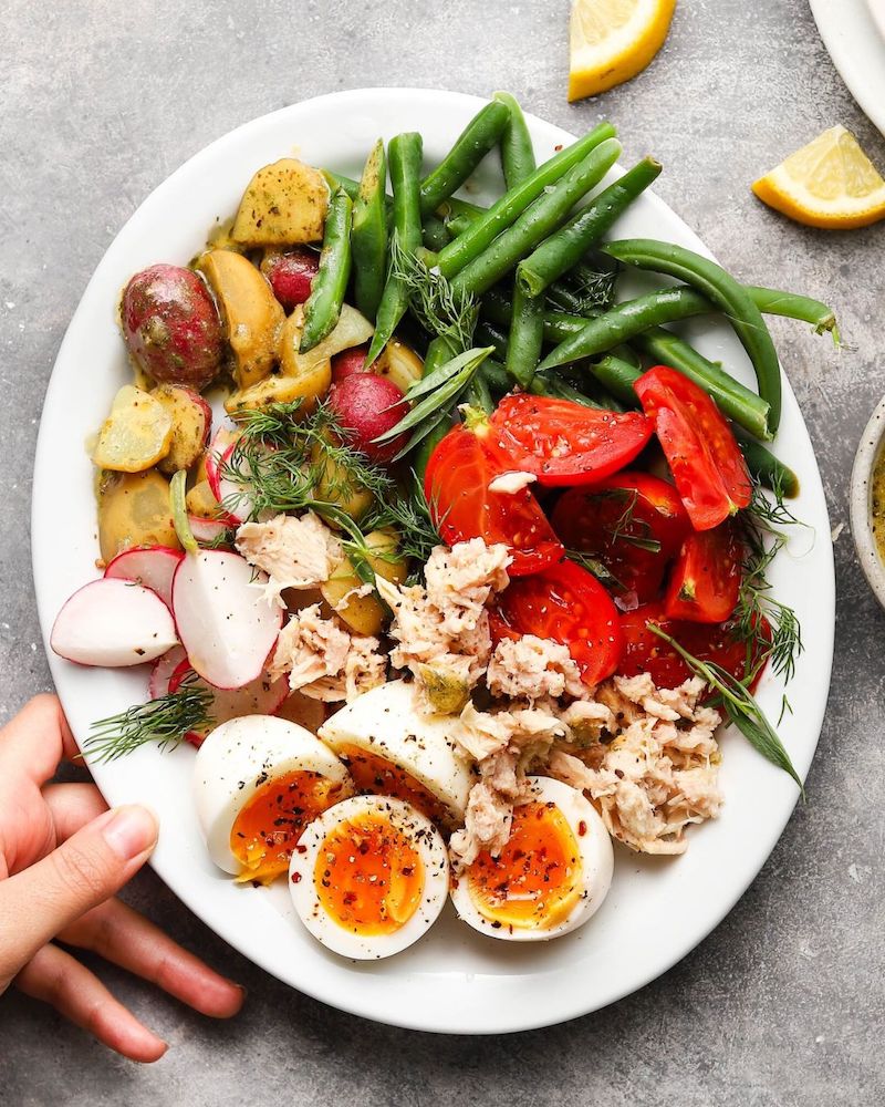 Niçoise salad with tuna, baby potatoes, green beans, jammy eggs, tomatoes, radishes, and Dijon lemon vinaigrette served on a white plate.