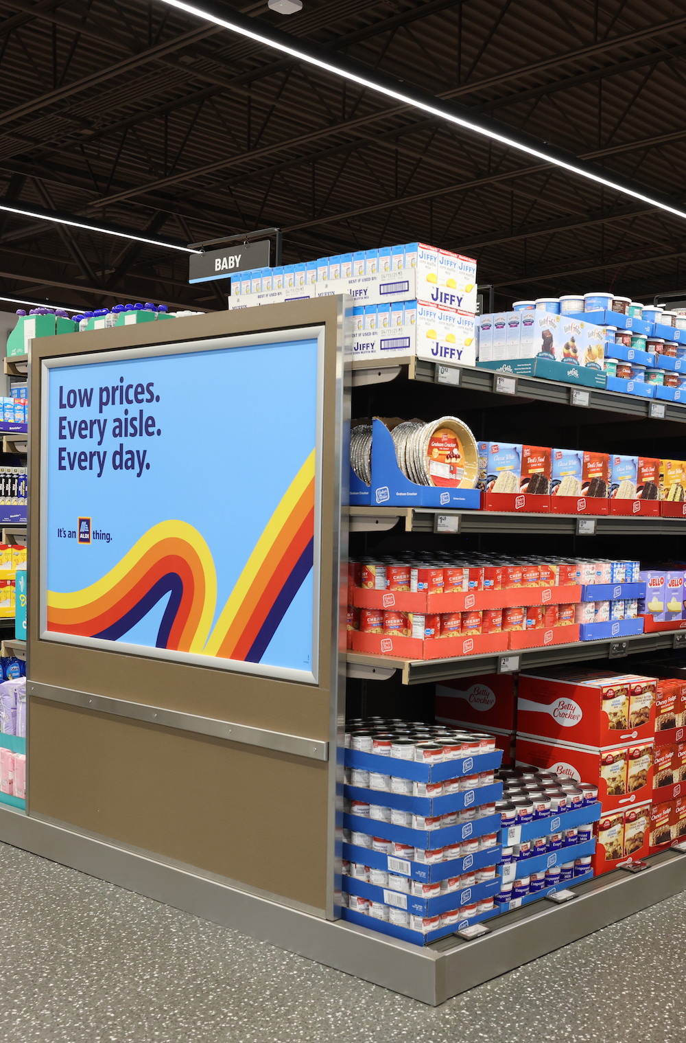 A visual example of the best things to buy at Aldi. Aldi grocery store aisle stocked with baking staples beside a bright sign reading “Low prices. Every aisle. Every day.”