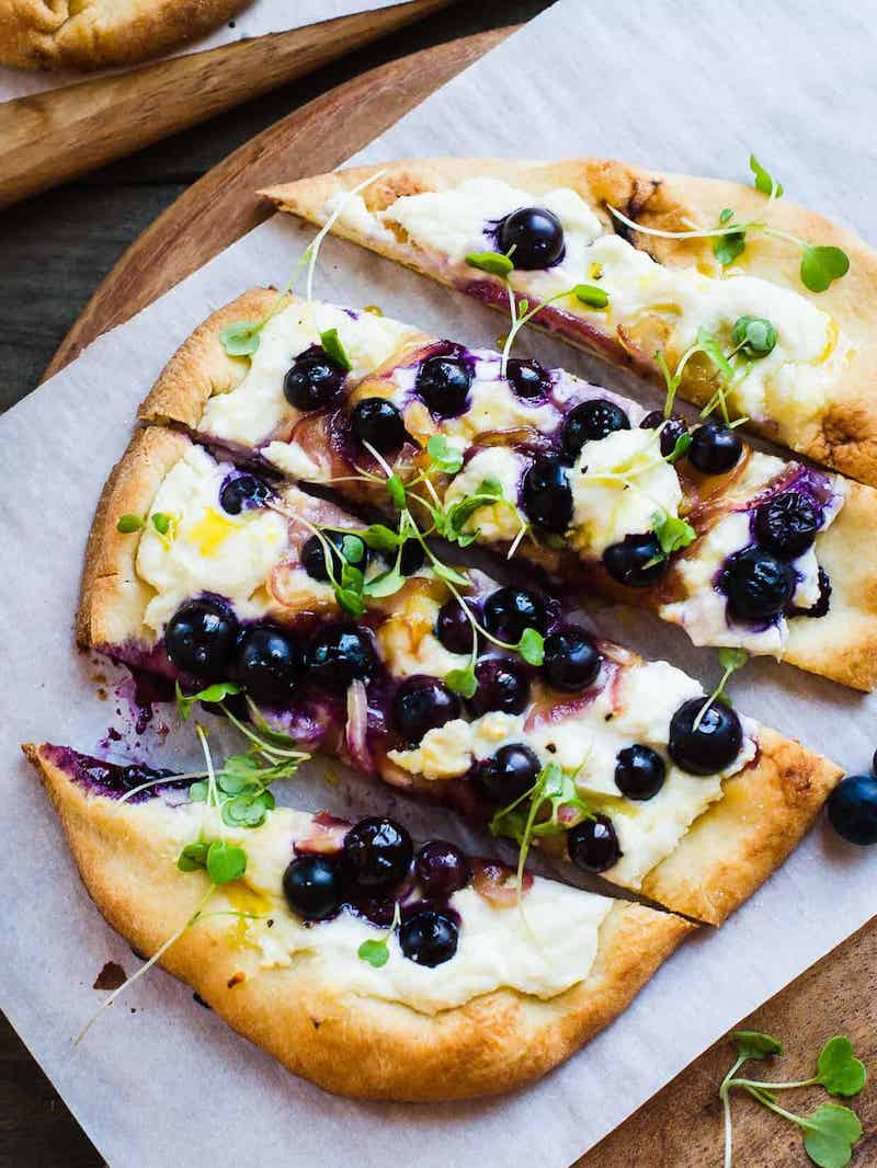 Blueberry, feta, and honey-caramelized onion naan pizza topped with fresh herbs.