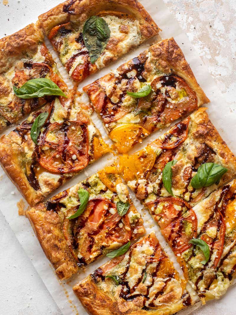 Caprese puff pastry topped with tomatoes, mozzarella, basil pesto, and balsamic glaze.