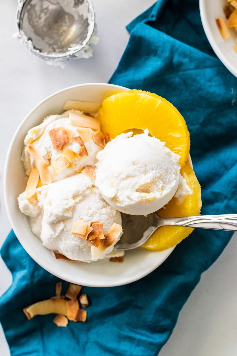 Dairy-free coconut rum ice cream topped with toasted coconut and served with fresh pineapple slices in a white bowl.