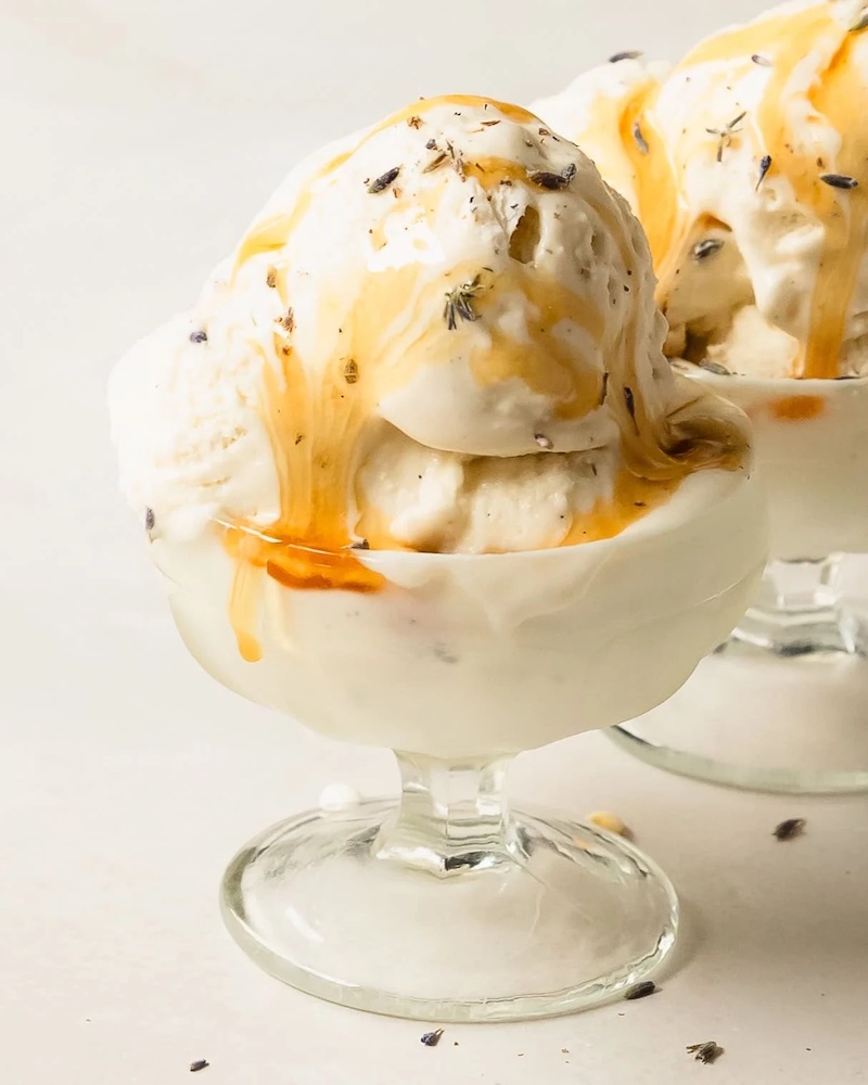 Creamy lavender ice cream drizzled with honey and sprinkled with dried culinary lavender in a glass dessert dish.
