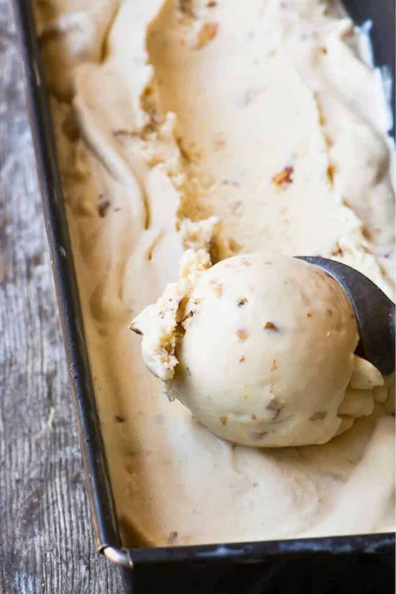 Scoop of homemade maple walnut ice cream with toasted walnut pieces in a loaf pan.