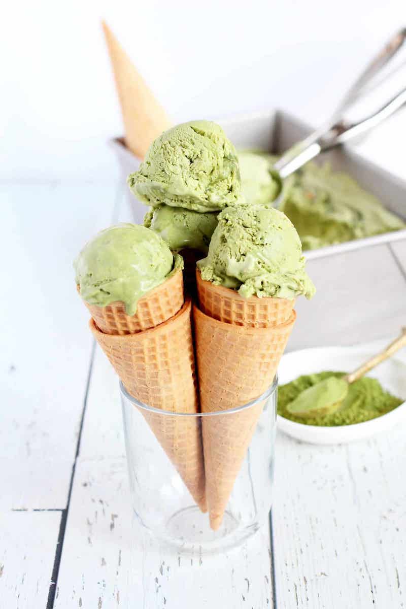 No-churn matcha green tea ice cream scooped into waffle cones with matcha powder and a loaf pan of homemade ice cream.