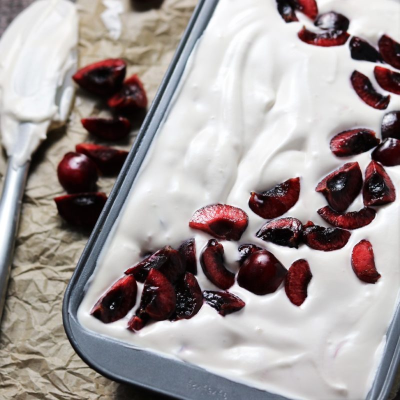 Creamy no-churn cherry vanilla ice cream topped with fresh cherries in a loaf pan, served with rich chocolate cherry sauce.