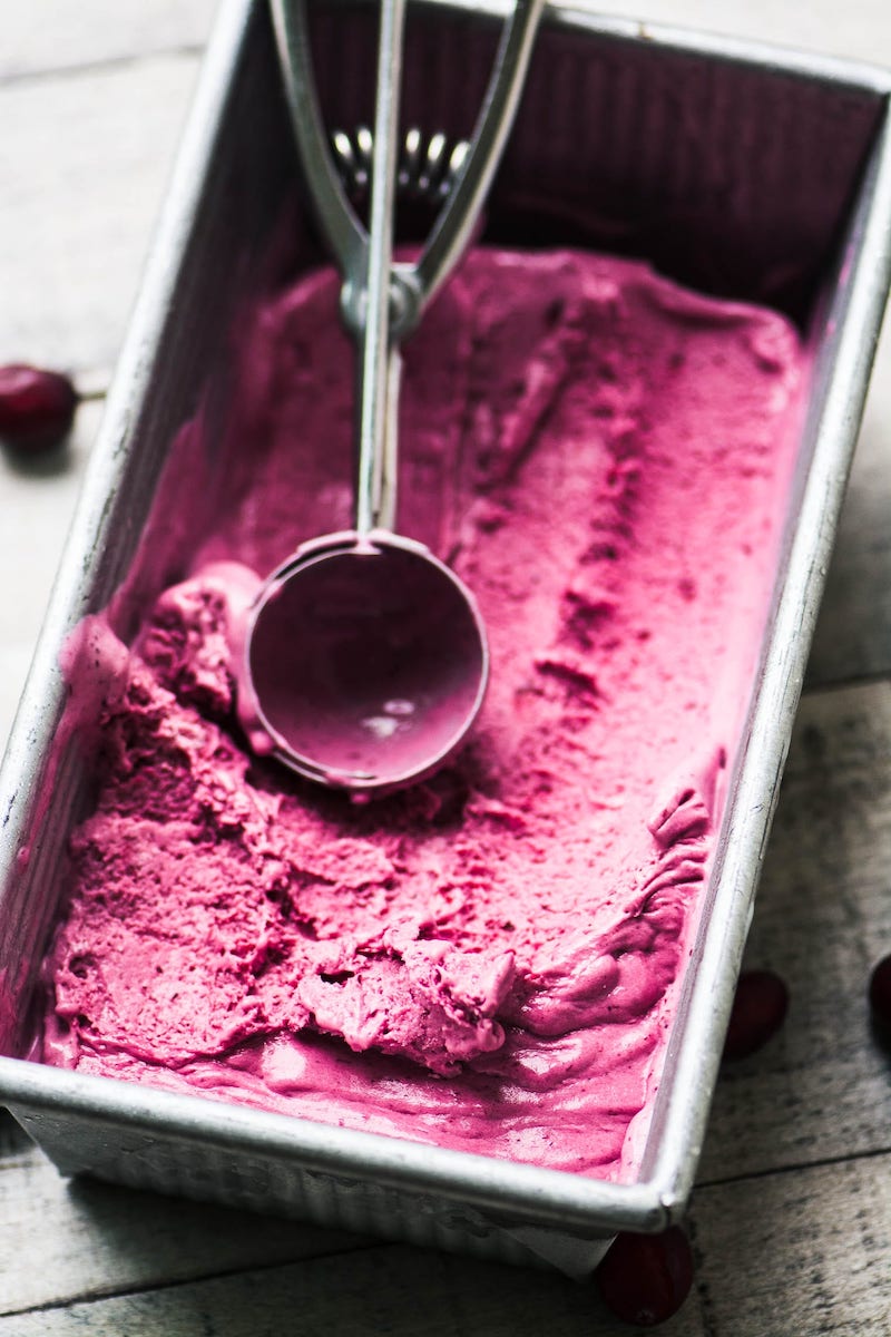 Creamy no-churn cranberry ice cream in a loaf pan with a metal ice cream scoop resting on top.
