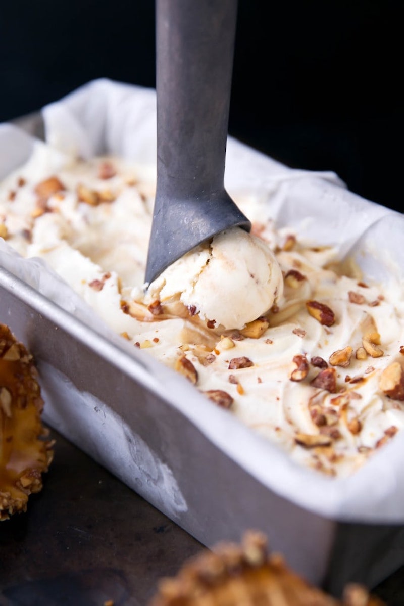 Creamy no-churn mascarpone ice cream swirled with salted caramel and topped with chopped almonds in a loaf pan with an ice cream scoop.