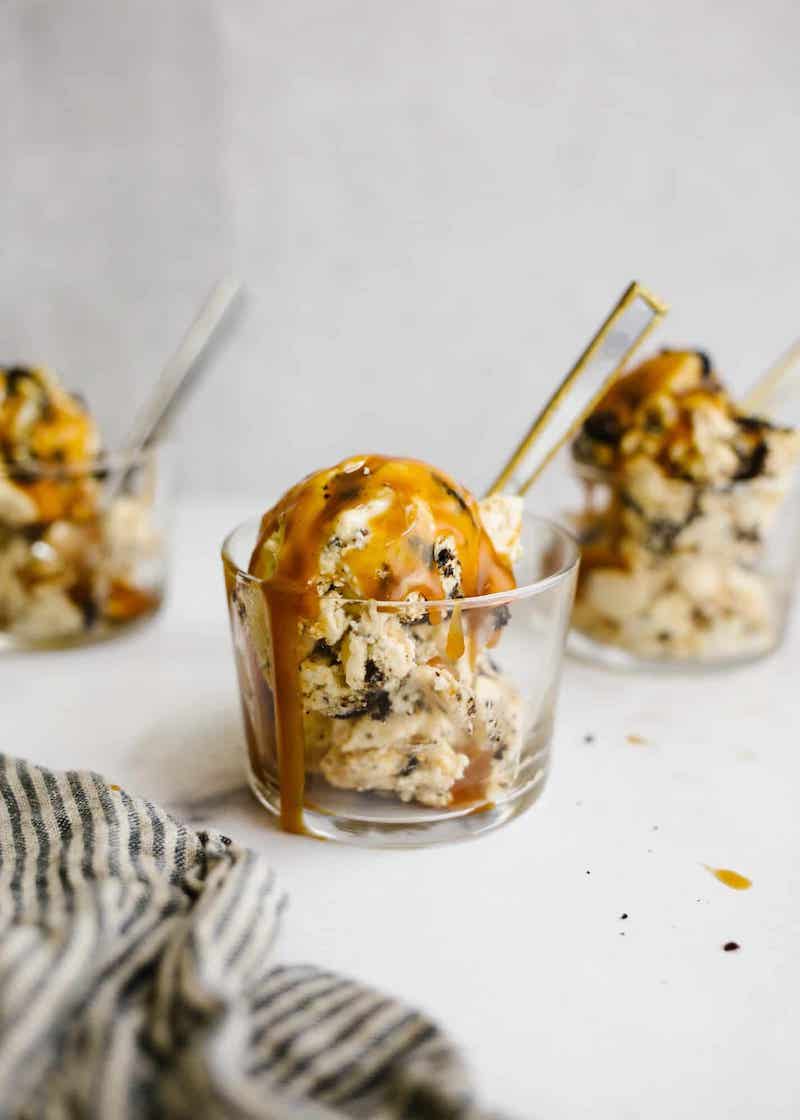 No-churn peanut butter caramel ice cream with crushed chocolate sandwich cookies and salted caramel sauce served in a glass dessert cup.