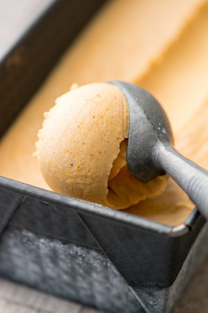 Creamy no-churn pumpkin spice ice cream in a loaf pan with an ice cream scoop lifting a perfectly round scoop.