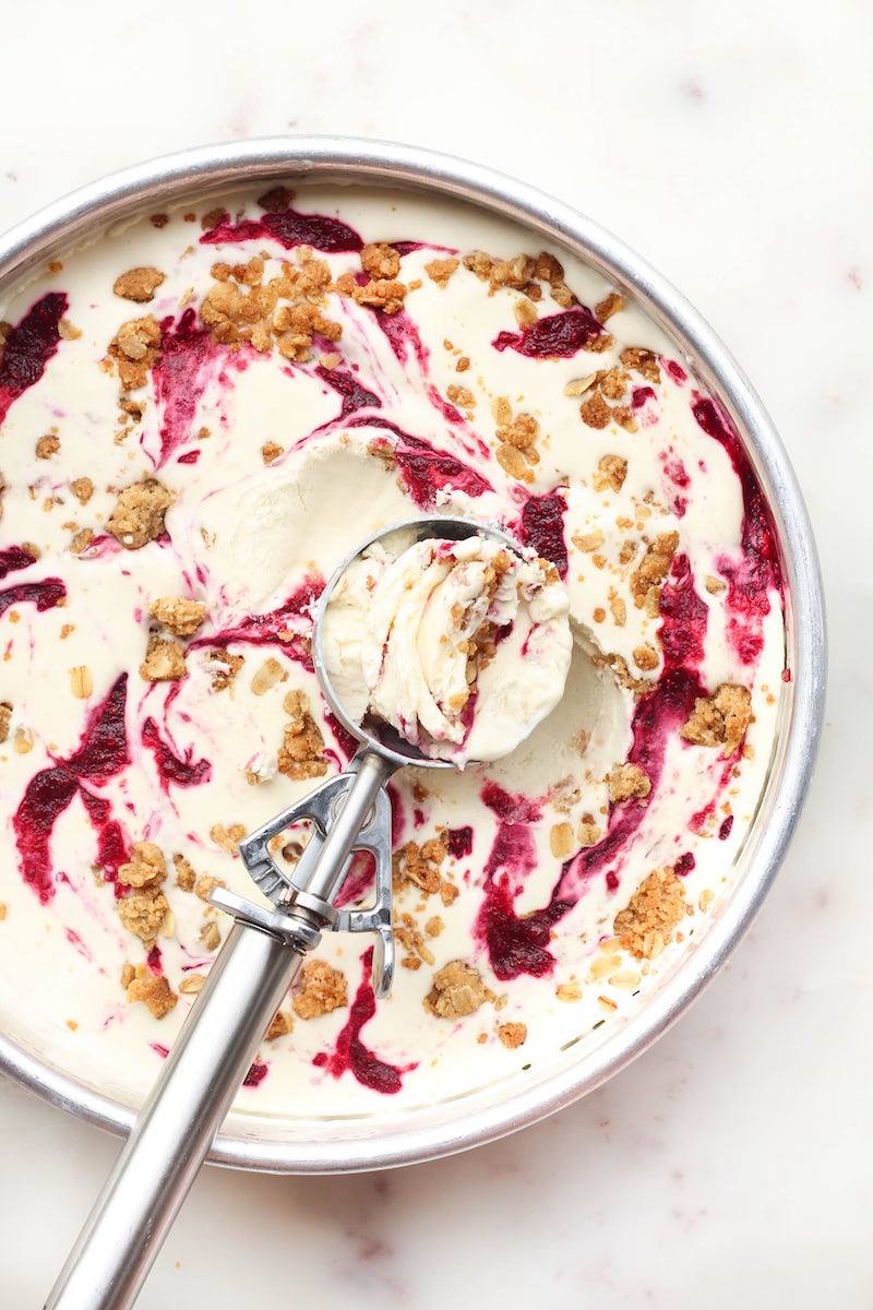 Overhead view of no-churn raspberry crisp ice cream swirled with raspberry sauce and buttery oat crumble in a round pan with an ice cream scoop.