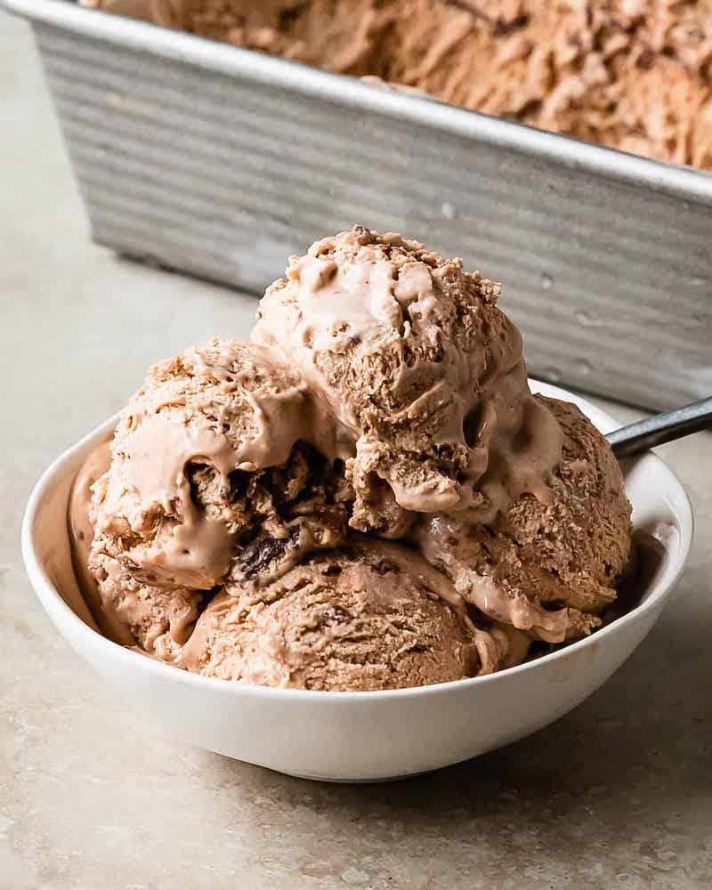 Bowl of creamy homemade Nutella ice cream with swirls of chocolate hazelnut spread and a loaf pan of ice cream in the background.