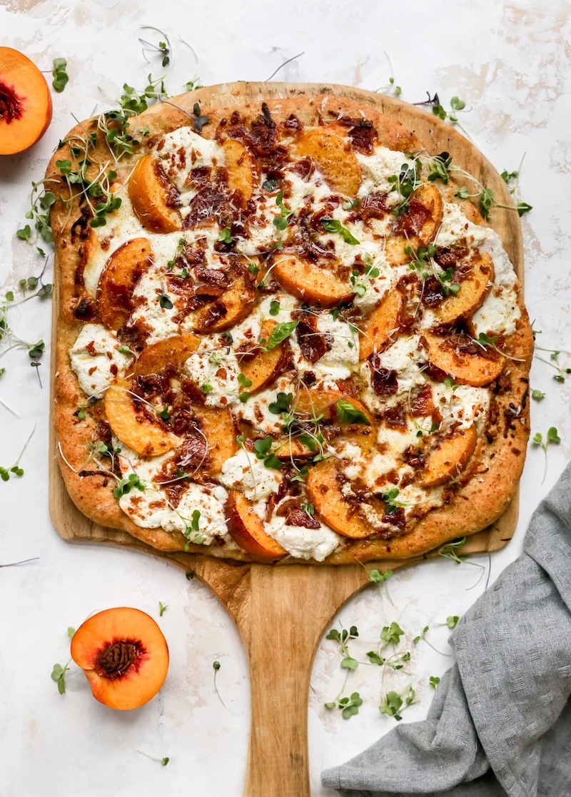 Peach and bacon white pizza topped with ricotta, melted cheese, and fresh herbs.