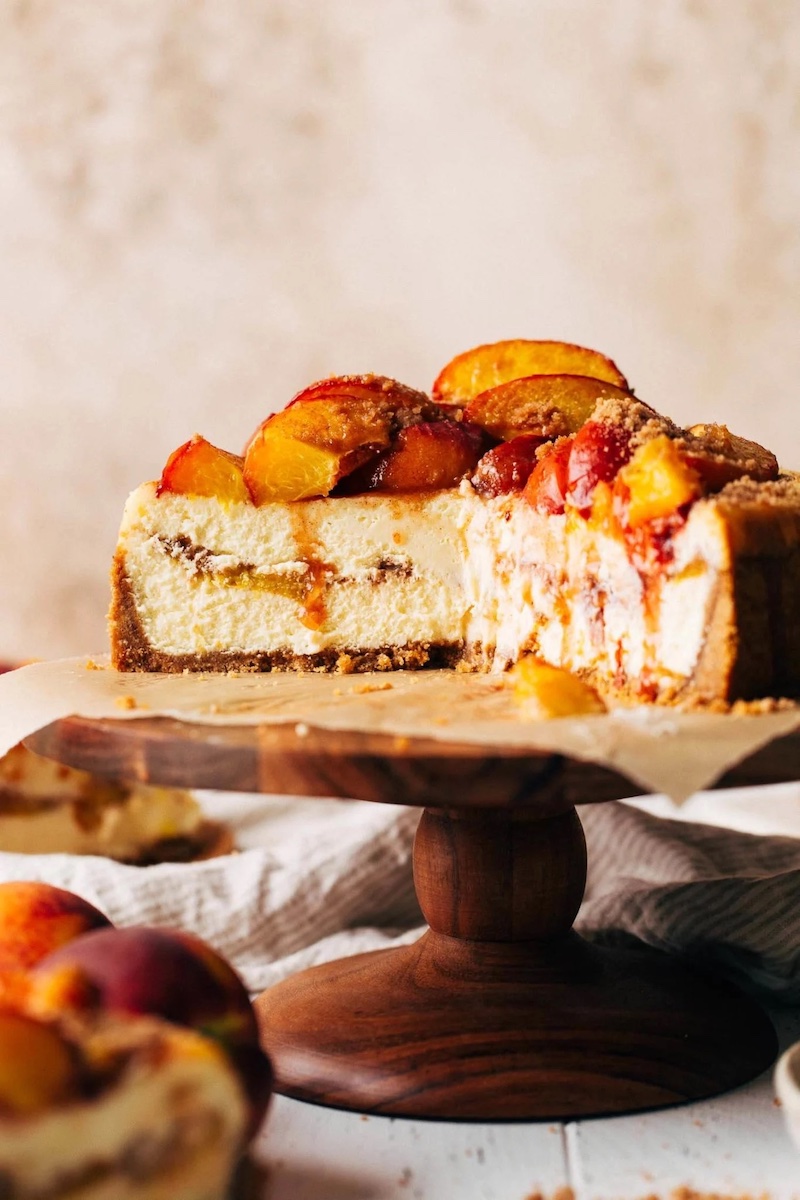 Inside view of peach cobbler cheesecake with a thick graham cracker crust, creamy vanilla cheesecake filling layered with tender peaches and buttery crumble, then topped with more roasted peaches.