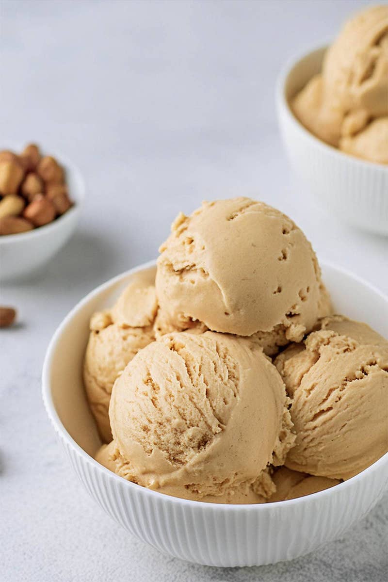 Creamy homemade peanut butter ice cream scooped into a white bowl with extra scoops in the background.
