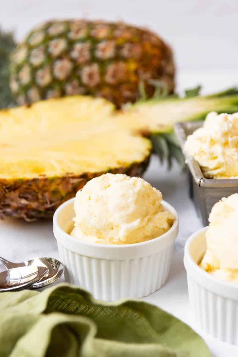Creamy homemade pineapple ice cream served in white ramekins with fresh pineapple halves in the background.