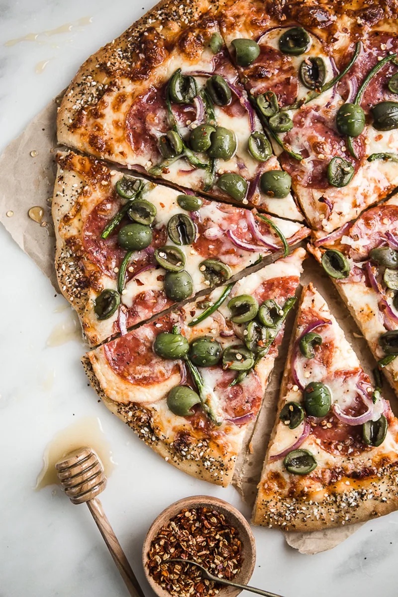 Salami pizza topped with jalapeños, olives, onions, and a drizzle of honey.