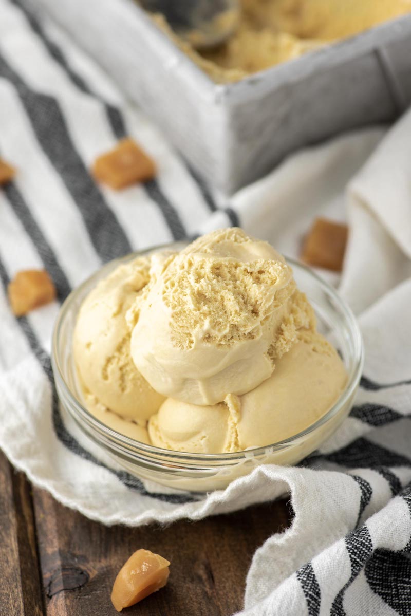 Creamy homemade salted caramel ice cream scooped into a glass bowl with soft caramel candies in the background.