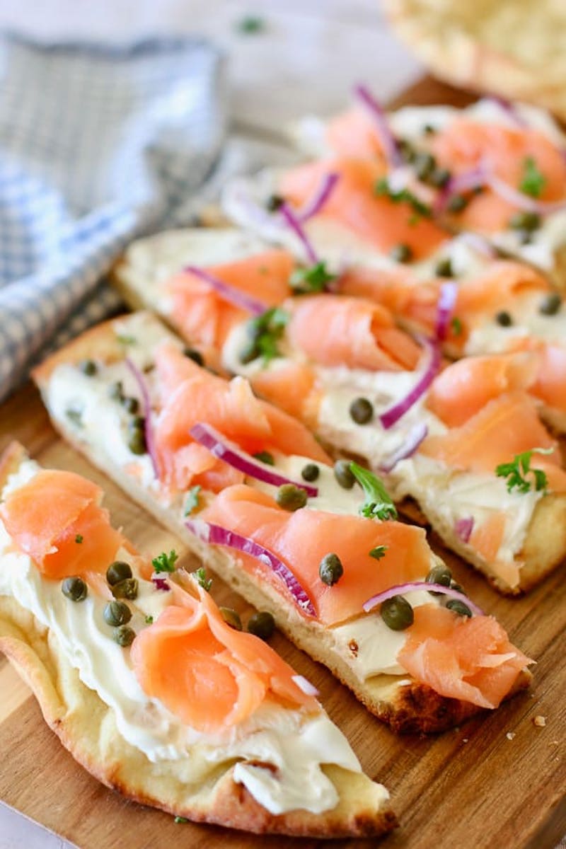 Smoked salmon pizza topped with cream cheese, capers, red onion, and fresh herbs.