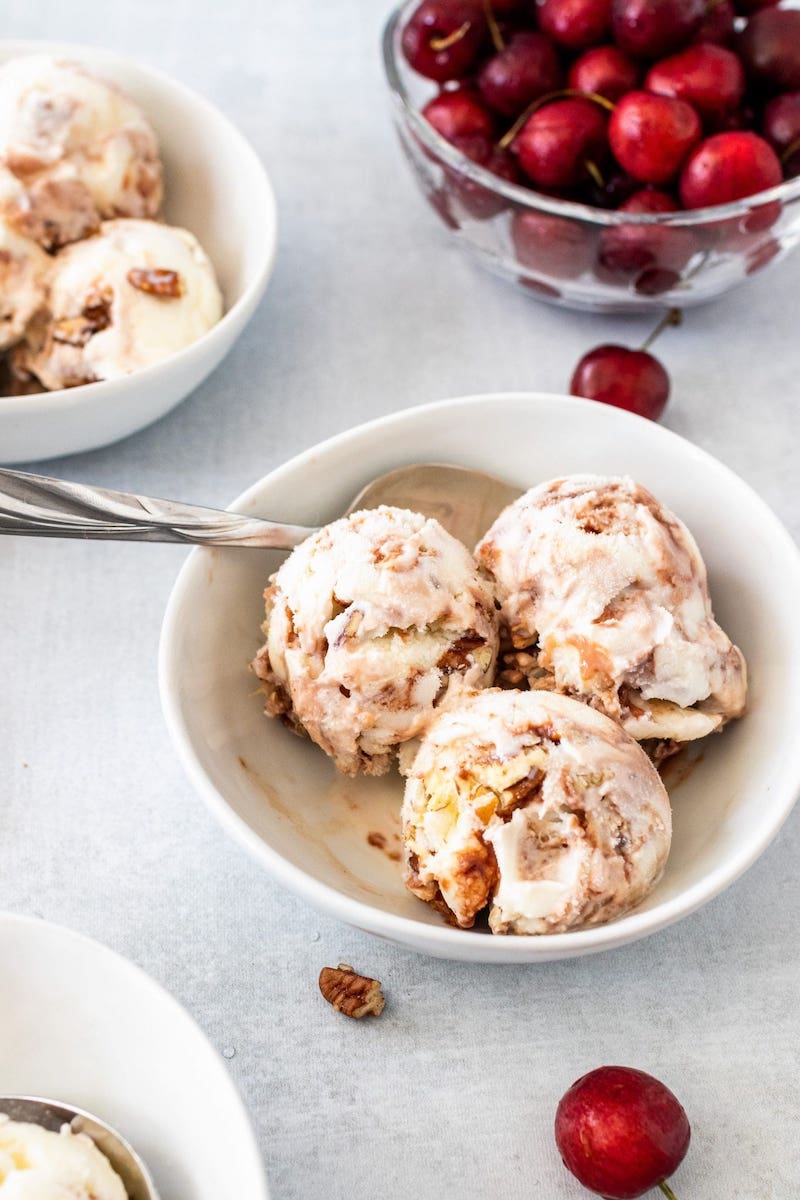 Homemade cherry ice cream swirled with tart cherry concentrate and chopped pecans, served in white bowls with fresh cherries on the table.